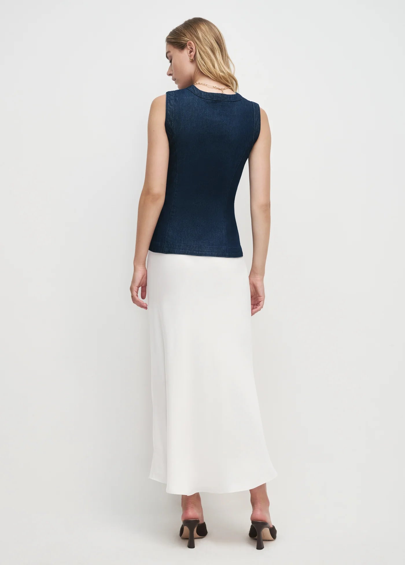Woman wearing a navy sleeveless top and white skirt on a white background