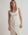 Woman wearing a white tank top and beige skirt against a plain background