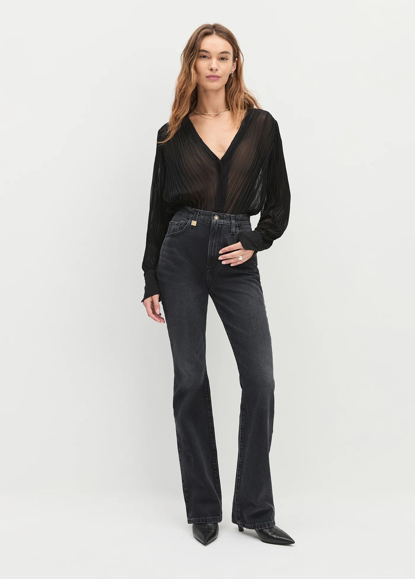 Woman wearing a black sheer top and black jeans on a white background, full body