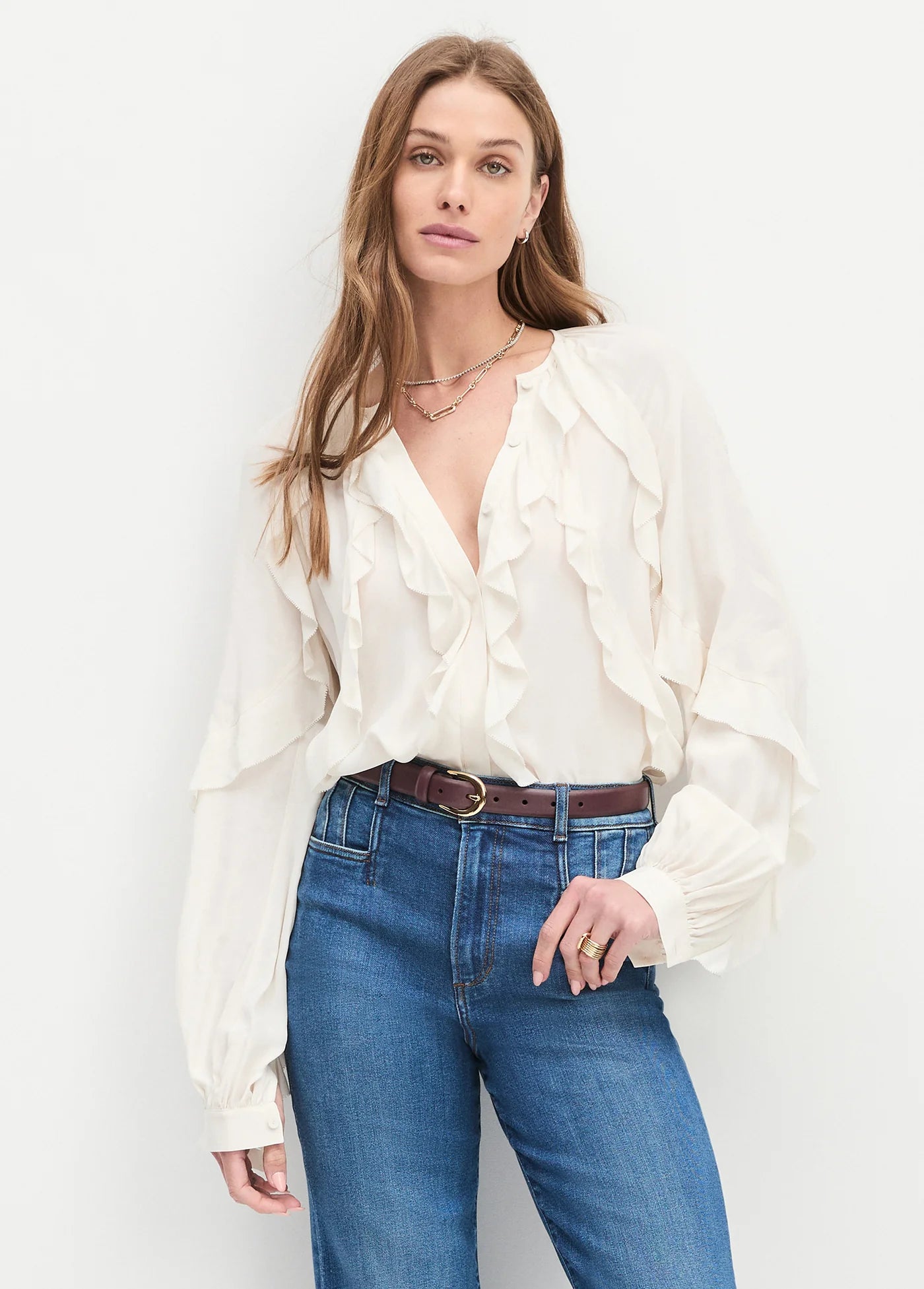 Woman wearing a white blouse and blue jeans against a plain background