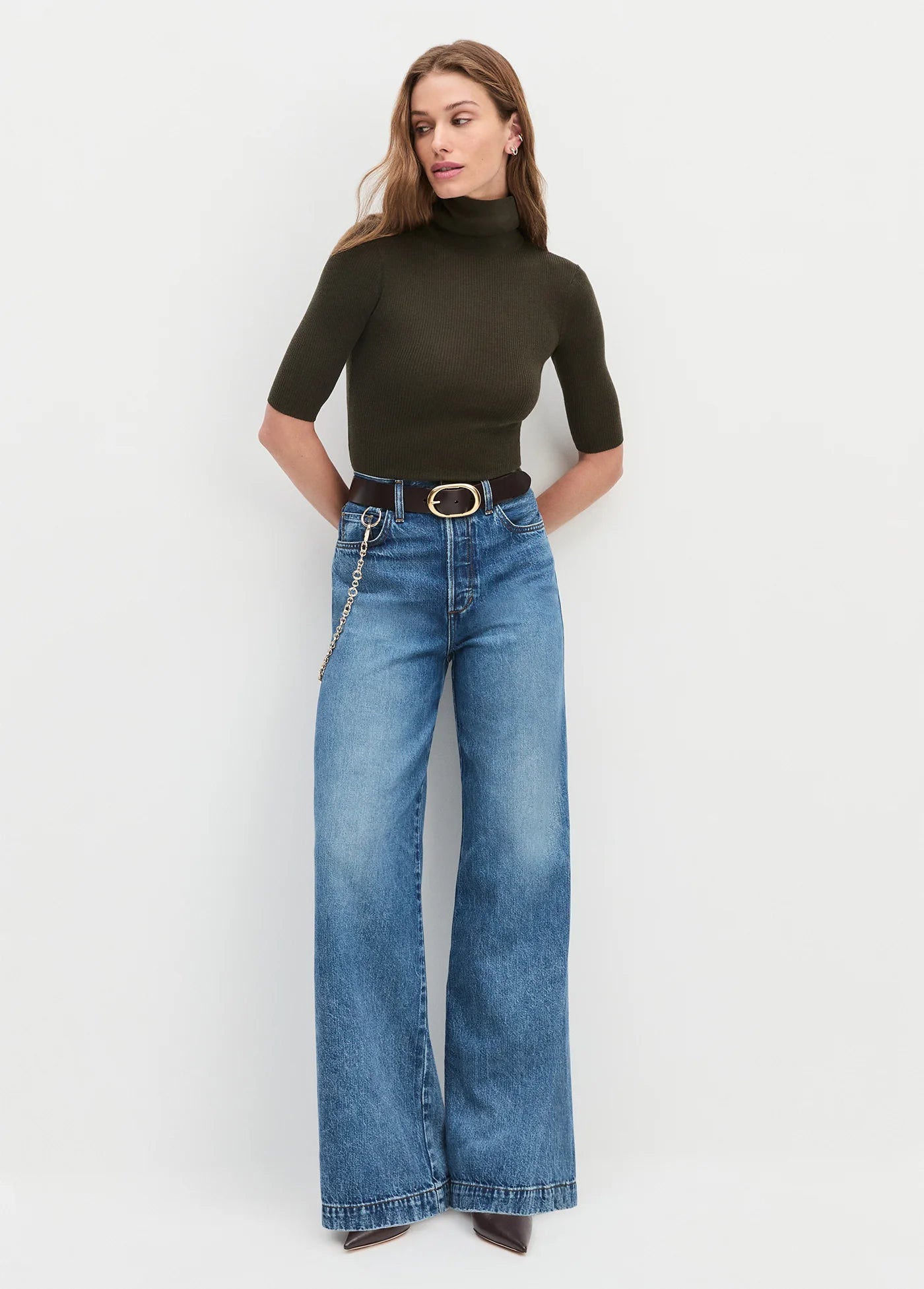 Woman wearing a green turtleneck and blue jeans against a white background