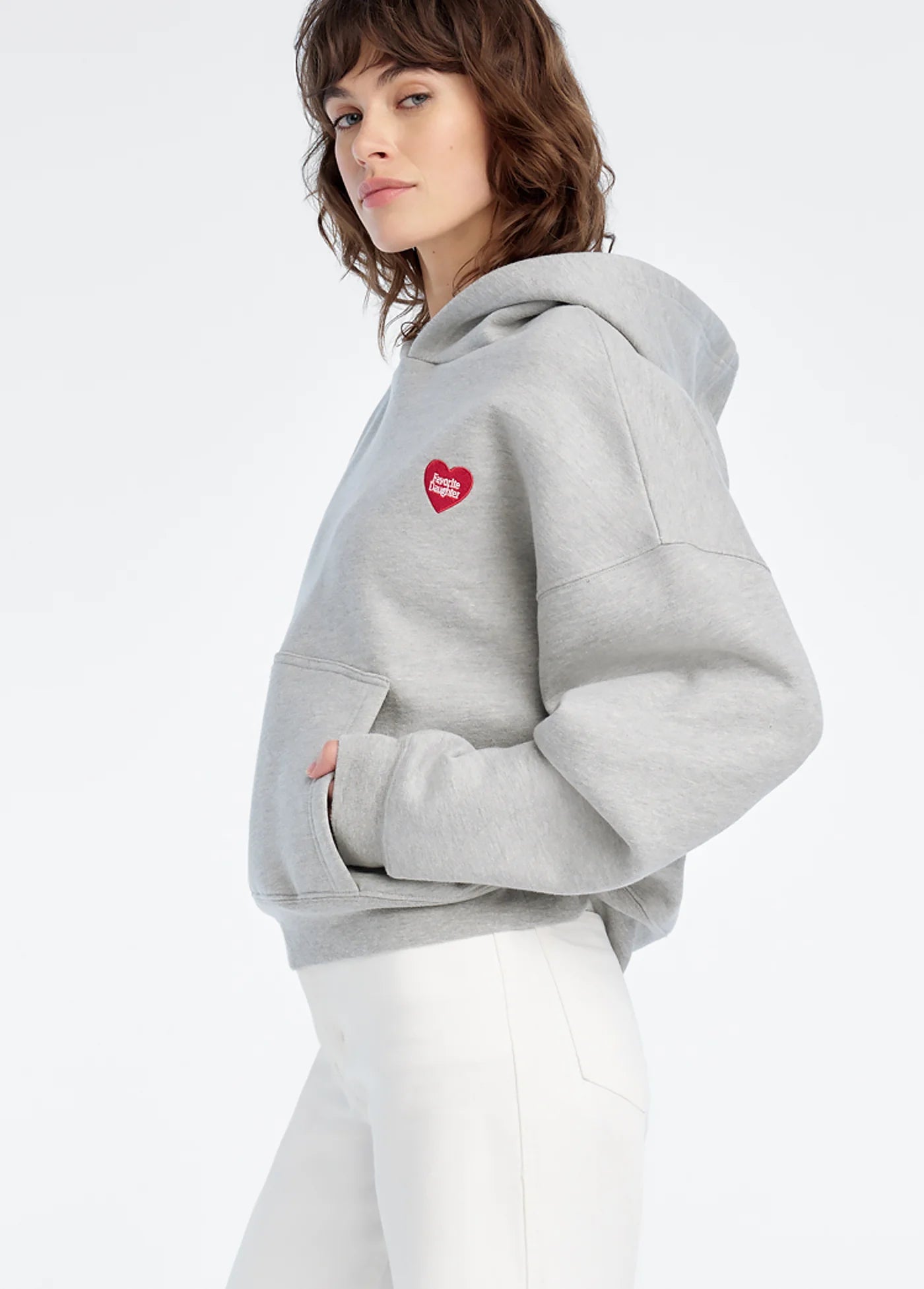 model wearing a grey hoodie with embroidered heart with white pants on a white background, side