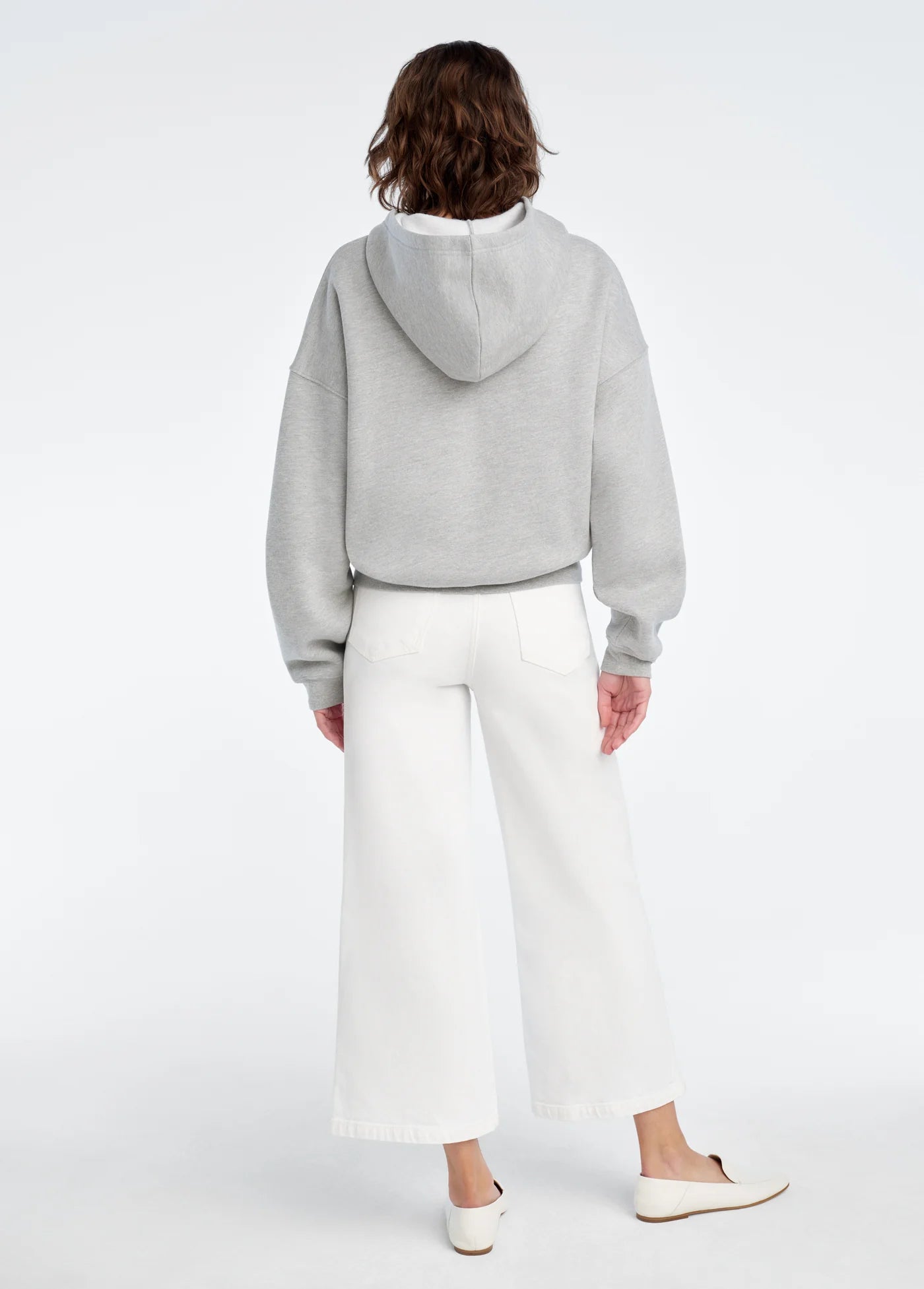 Person wearing a gray hoodie and white pants on a white background