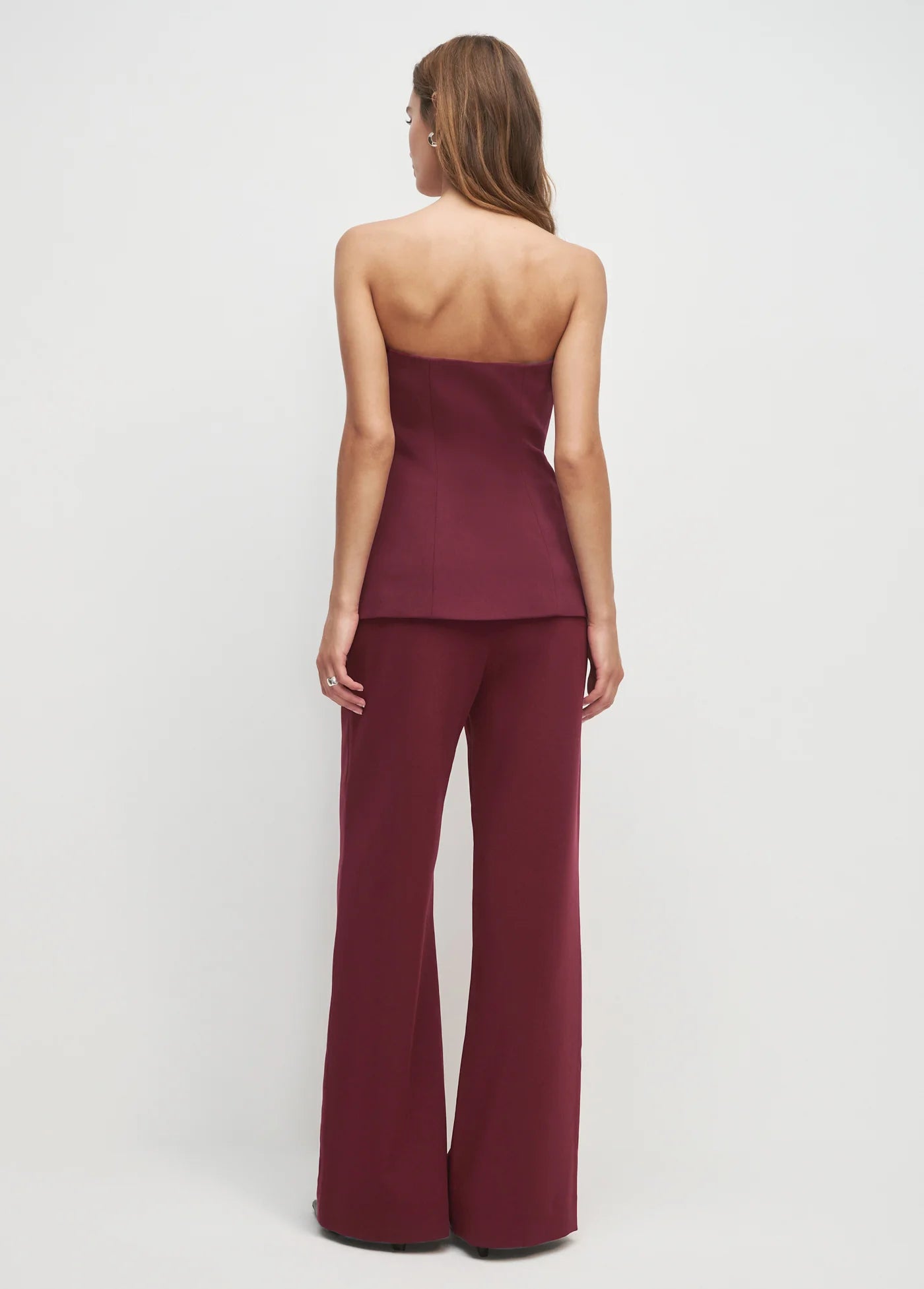 Woman wearing a burgundy strapless top and wide-leg pants on a white background