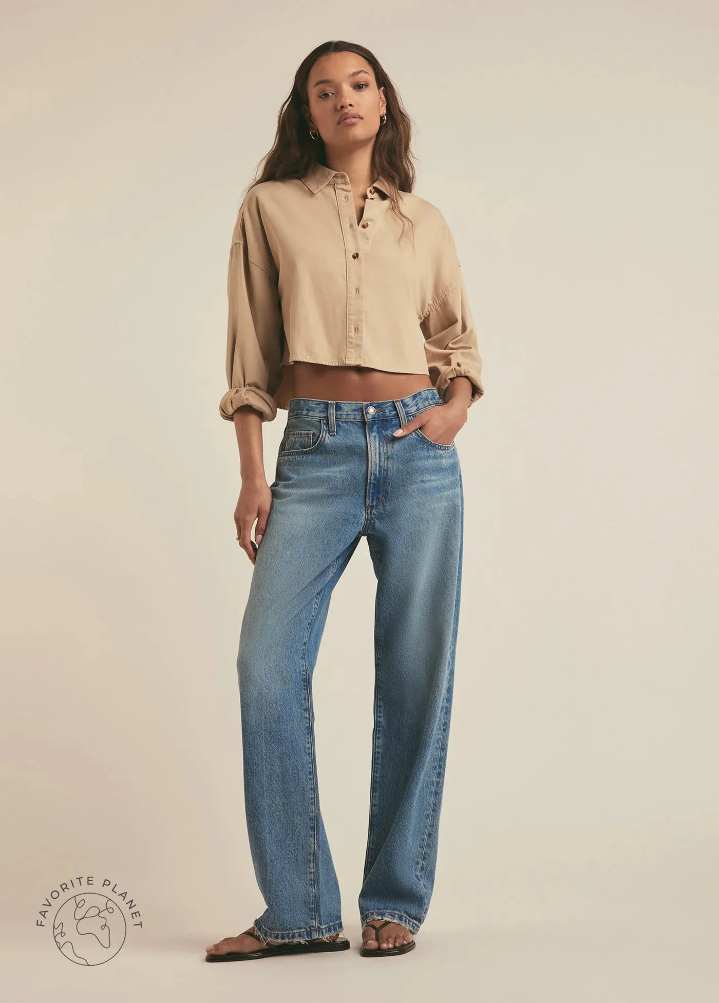 Woman wearing a beige shirt and blue jeans on a plain background