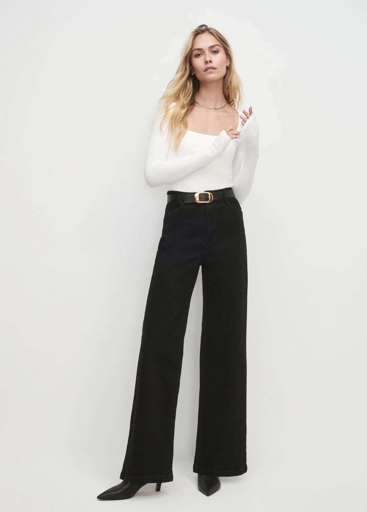 Woman wearing a white top and black pants against a white background