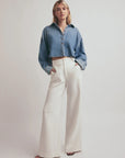 Person wearing a blue denim shirt and white pants on a plain background