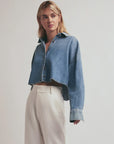 Woman wearing a blue denim jacket and white pants on a plain background