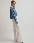 Person wearing a denim jacket and white pants on a plain background
