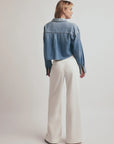 Person wearing a blue denim jacket and white pants on a plain background