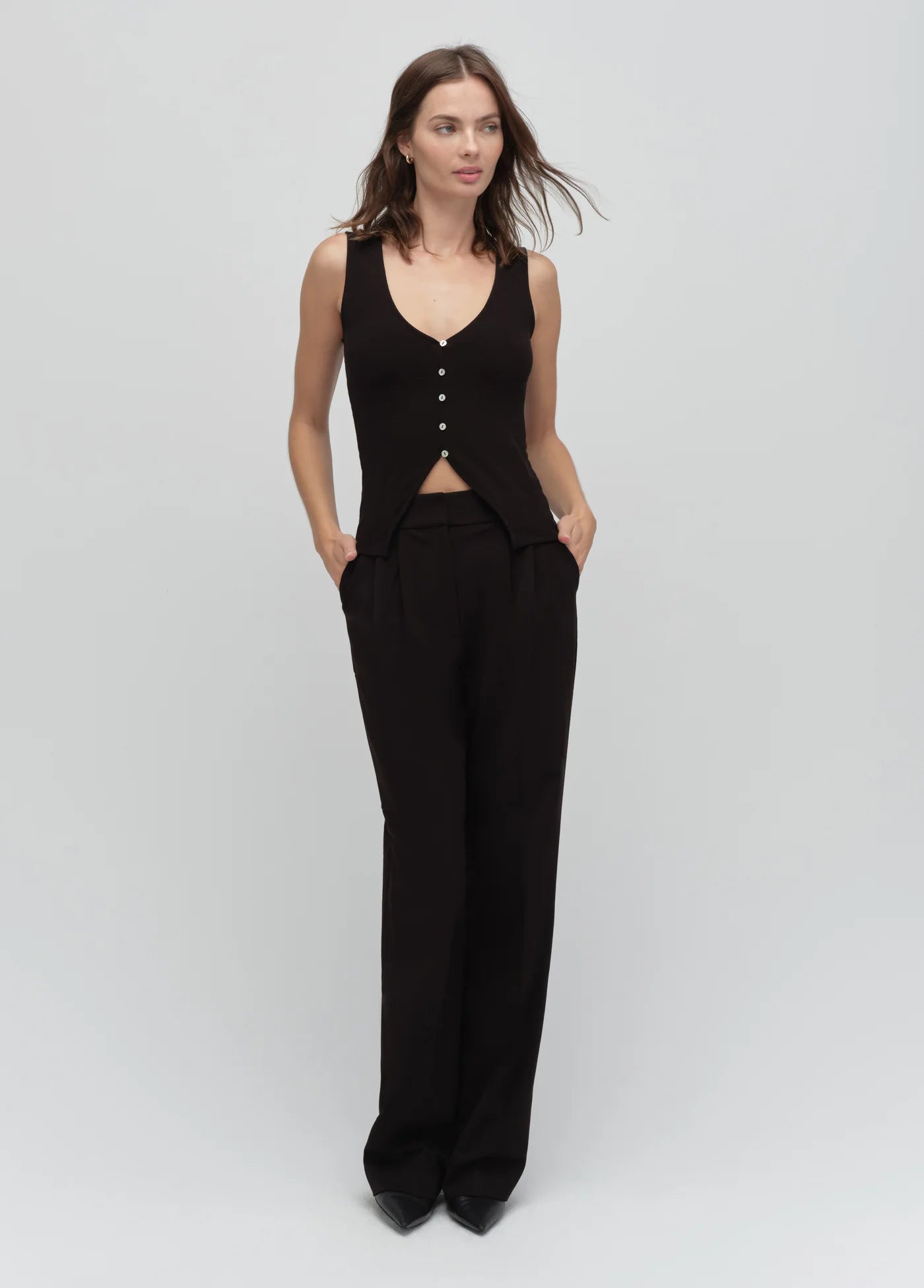 Woman wearing a black sleeveless top and wide-leg pants on a light gray background