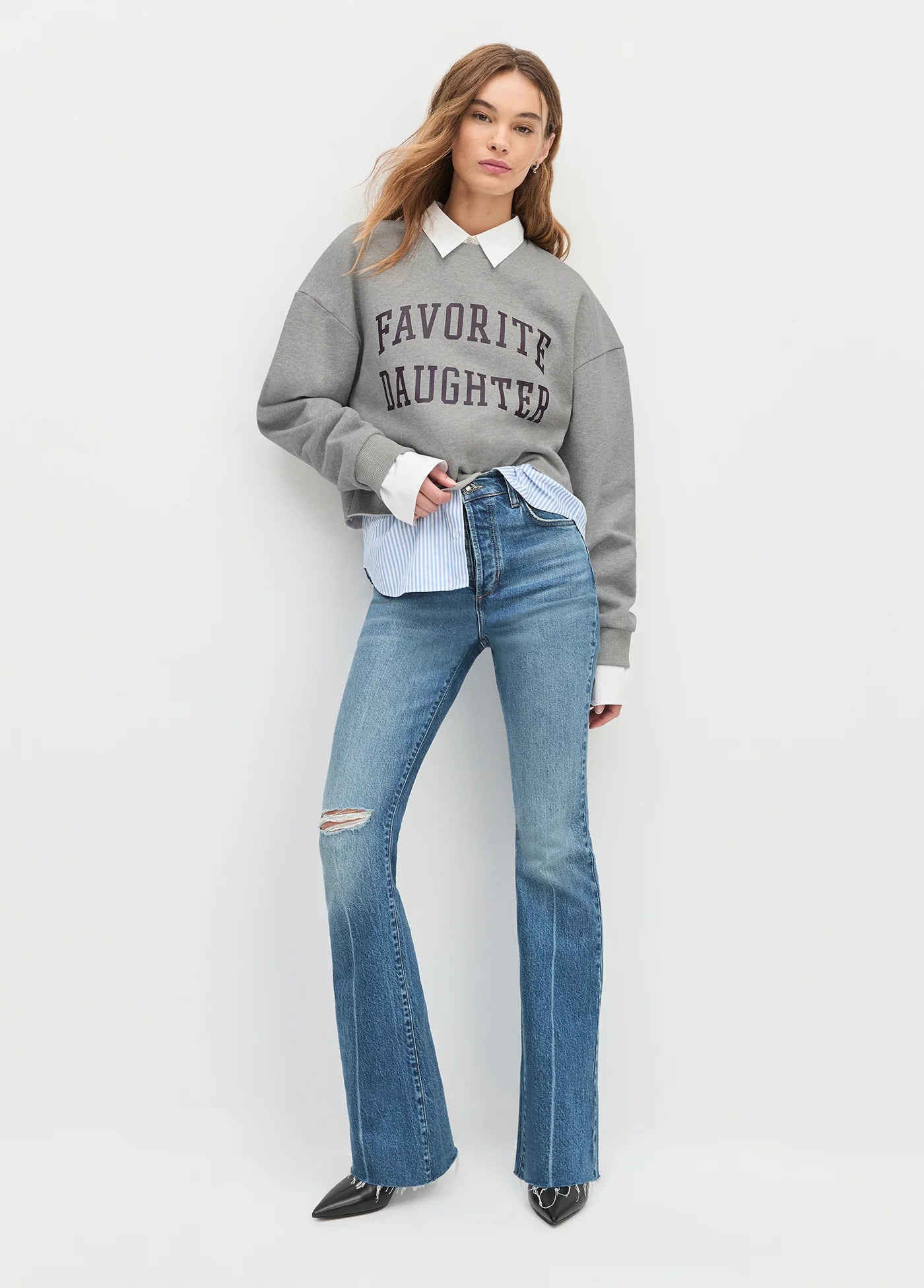 Woman wearing a gray sweater with 'Favorite Daughter' text and blue jeans on a white background front view