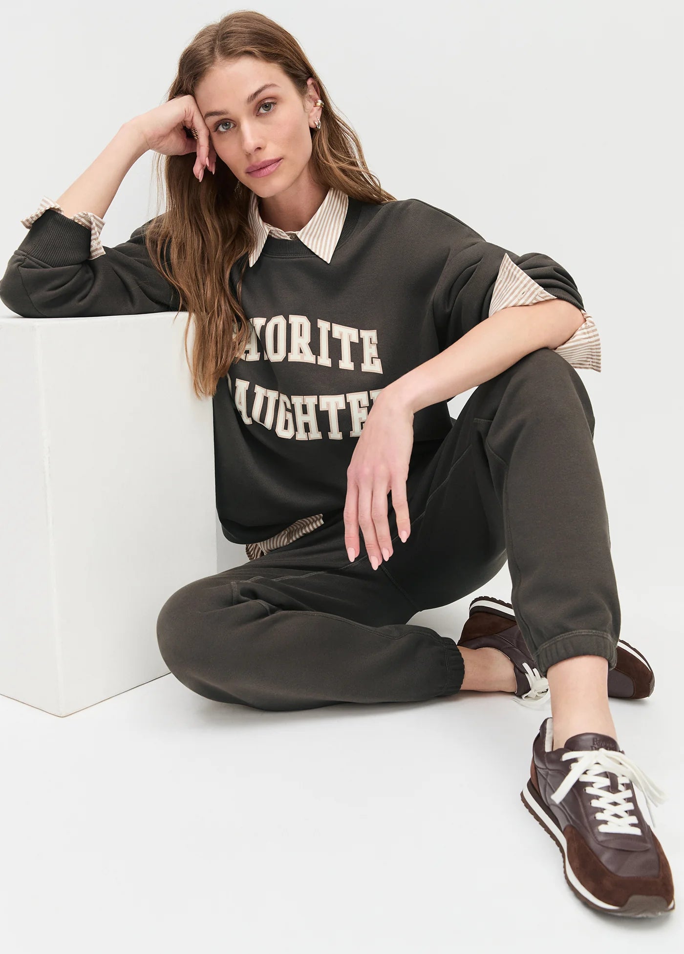 model wearing collegiate sweatshirt with brown pants and brown shoes sitting on the ground with a white background