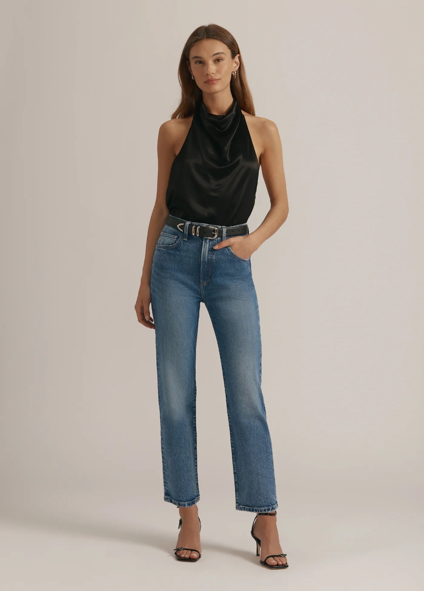 Woman wearing a black halter top and blue jeans on a beige background