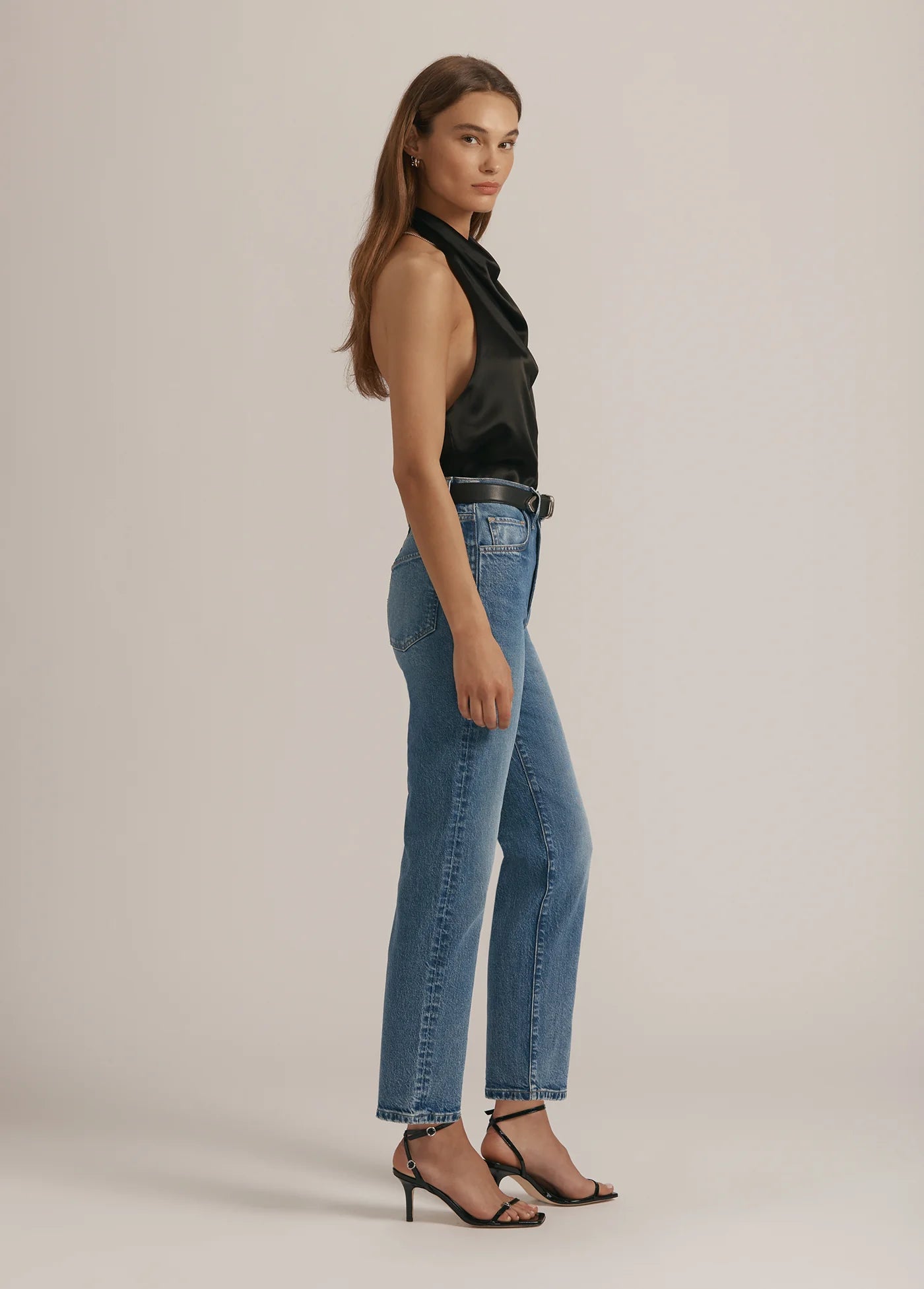 Woman wearing a black top and blue jeans on a plain background
