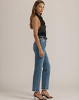 Woman wearing a black top and blue jeans on a plain background