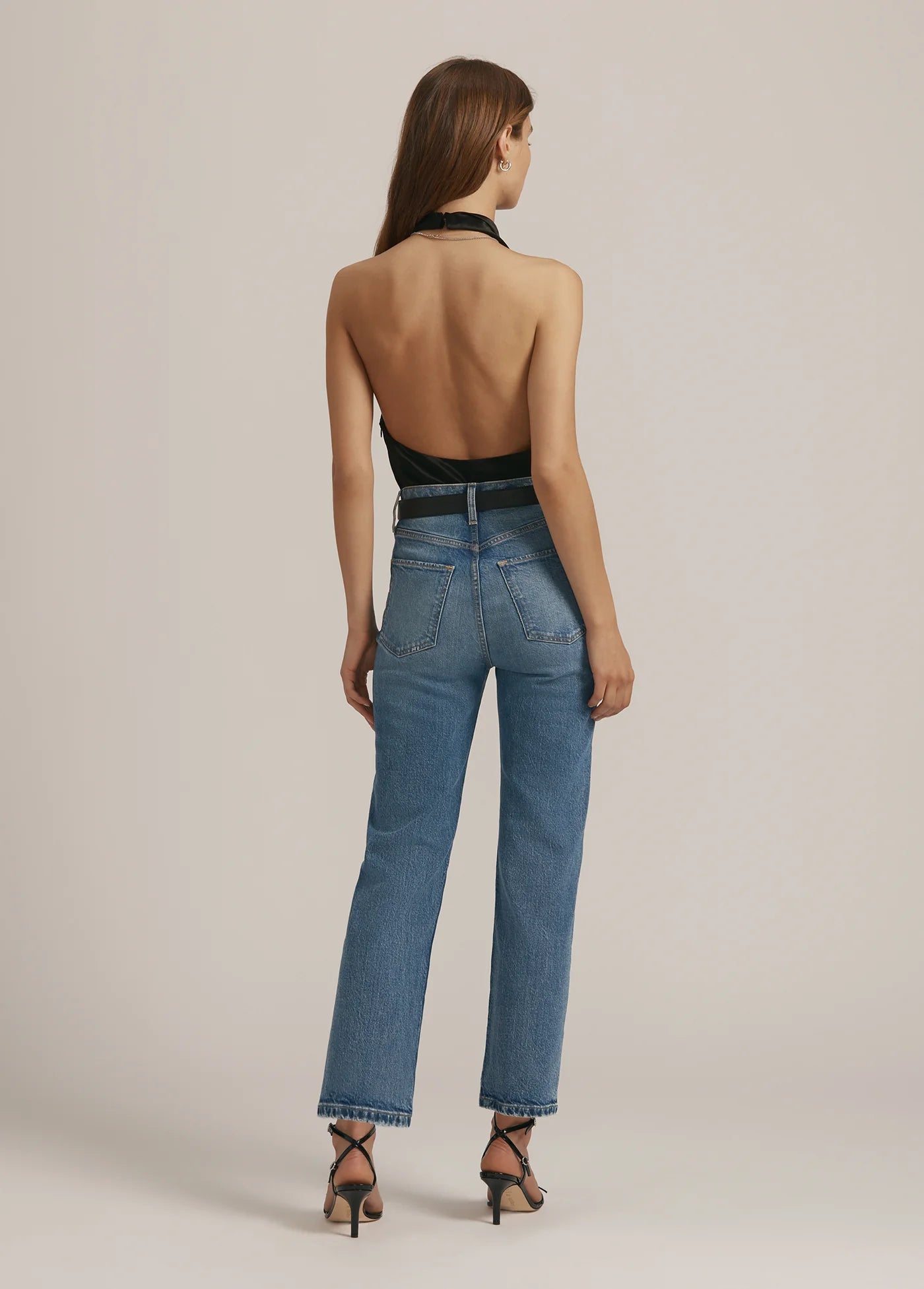 Woman wearing blue jeans and a black open-back top on a beige background