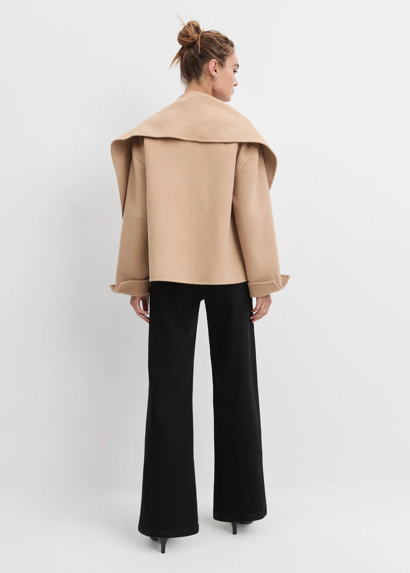 Woman wearing a beige coat and black pants on a white background back view