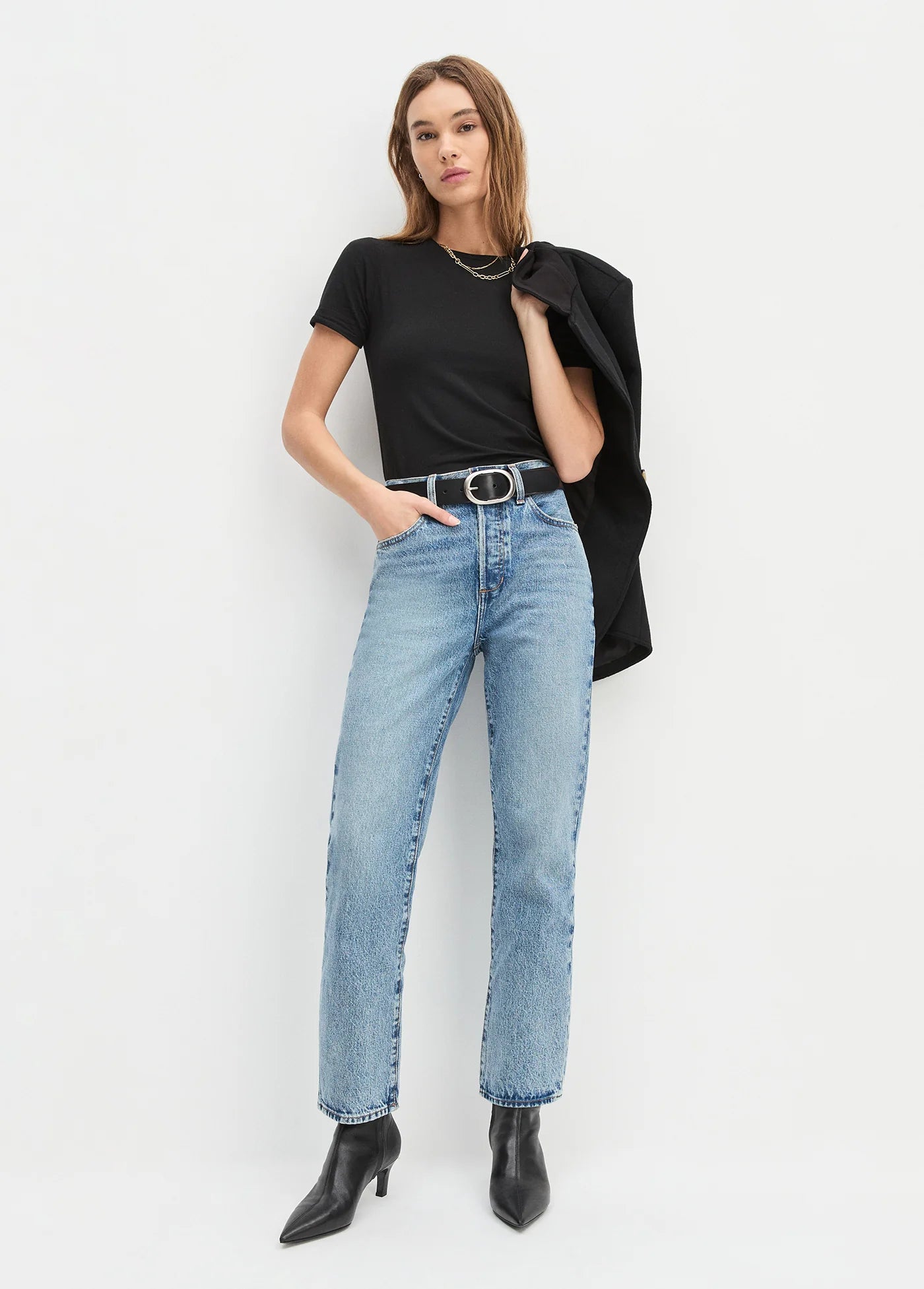 Woman wearing a black t-shirt, light blue jeans, and black boots on a white background