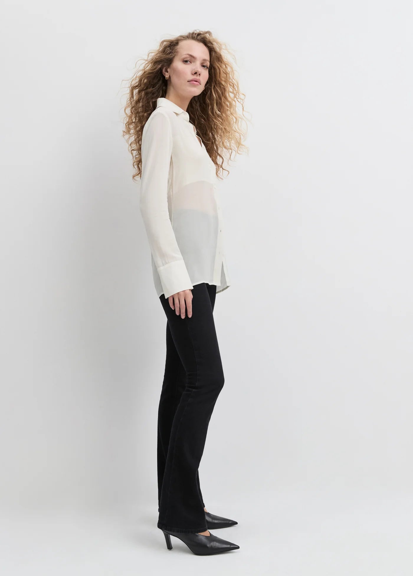 Woman wearing a white blouse and black pants against a plain background