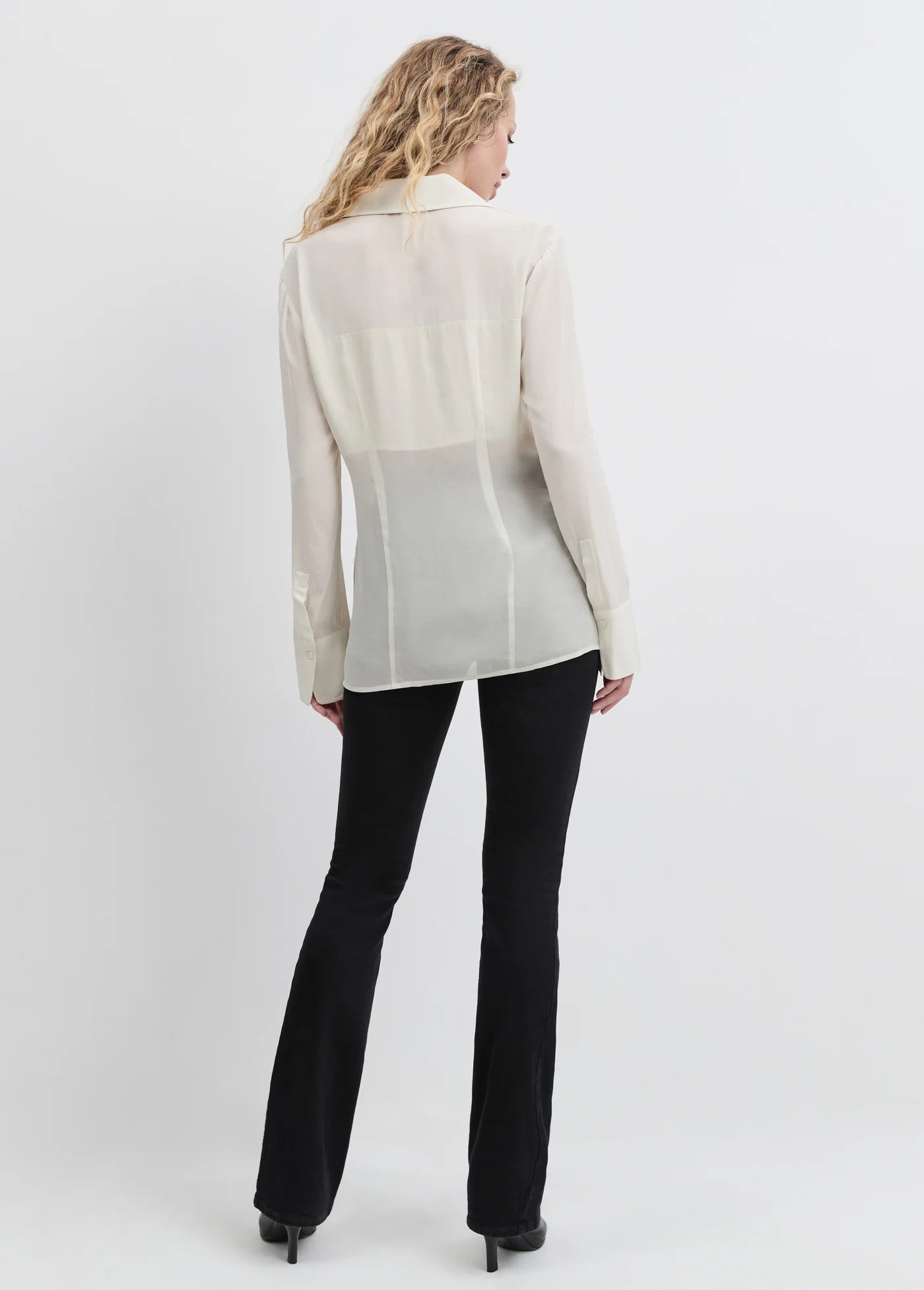 Woman wearing a light-colored blouse and black pants on a white background