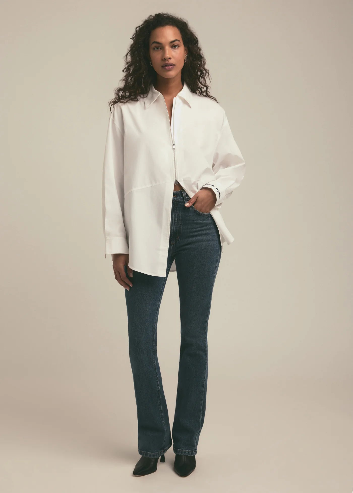 Woman wearing a white shirt and blue jeans against a beige background, full body front