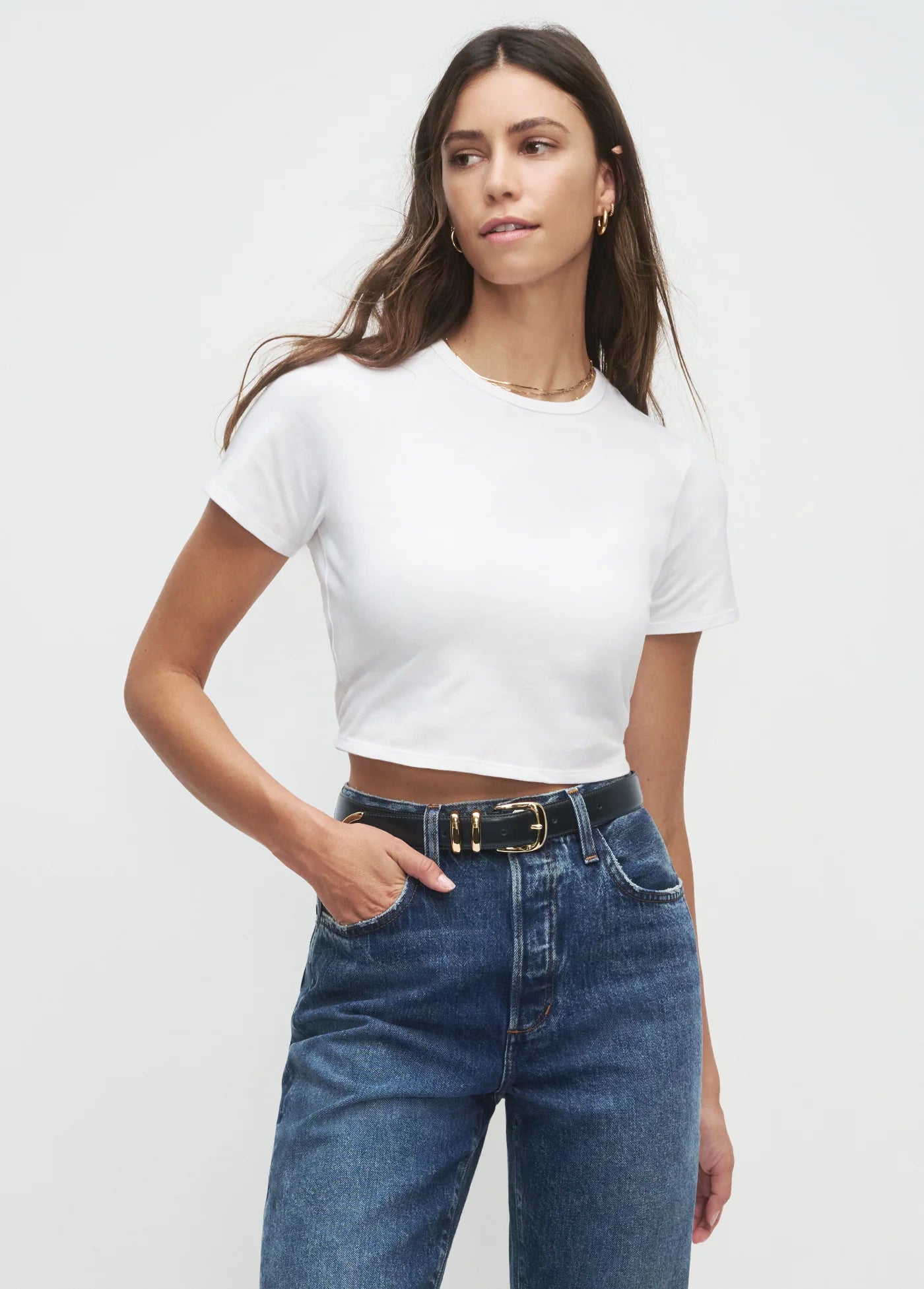 Woman wearing a white t-shirt and blue jeans against a plain background