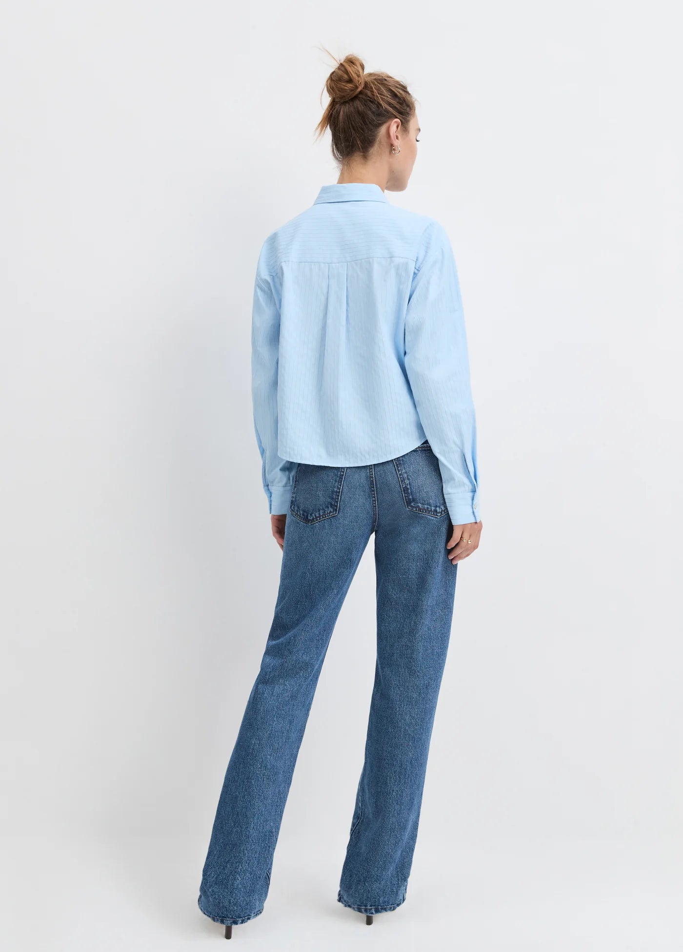 Model wearing the light blue stripe jenni top with jean and heels on a white background, back view