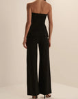 A woman shown from the back wearing a black strapless peplum top and matching wide-leg trousers, photographed in a clean studio setting.