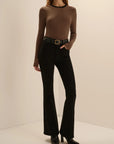 A model wearing a brown and black striped long-sleeve top, black flared pants, and black pointed-toe heels, standing against a plain beige studio background.