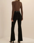 A model shown from the back wearing a brown and black striped long-sleeve mock neck top, black flared jeans, and black heels, set against a plain beige studio background.