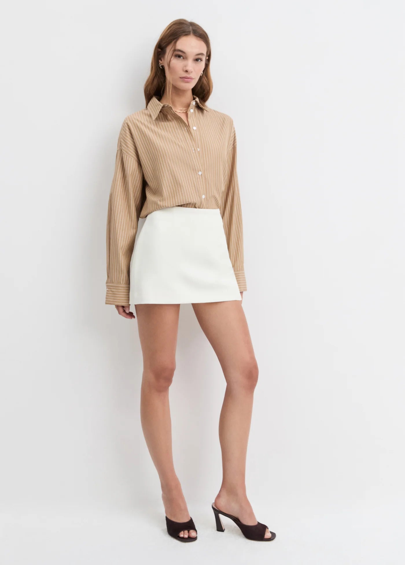 Woman wearing a beige blouse and white skirt on a plain background