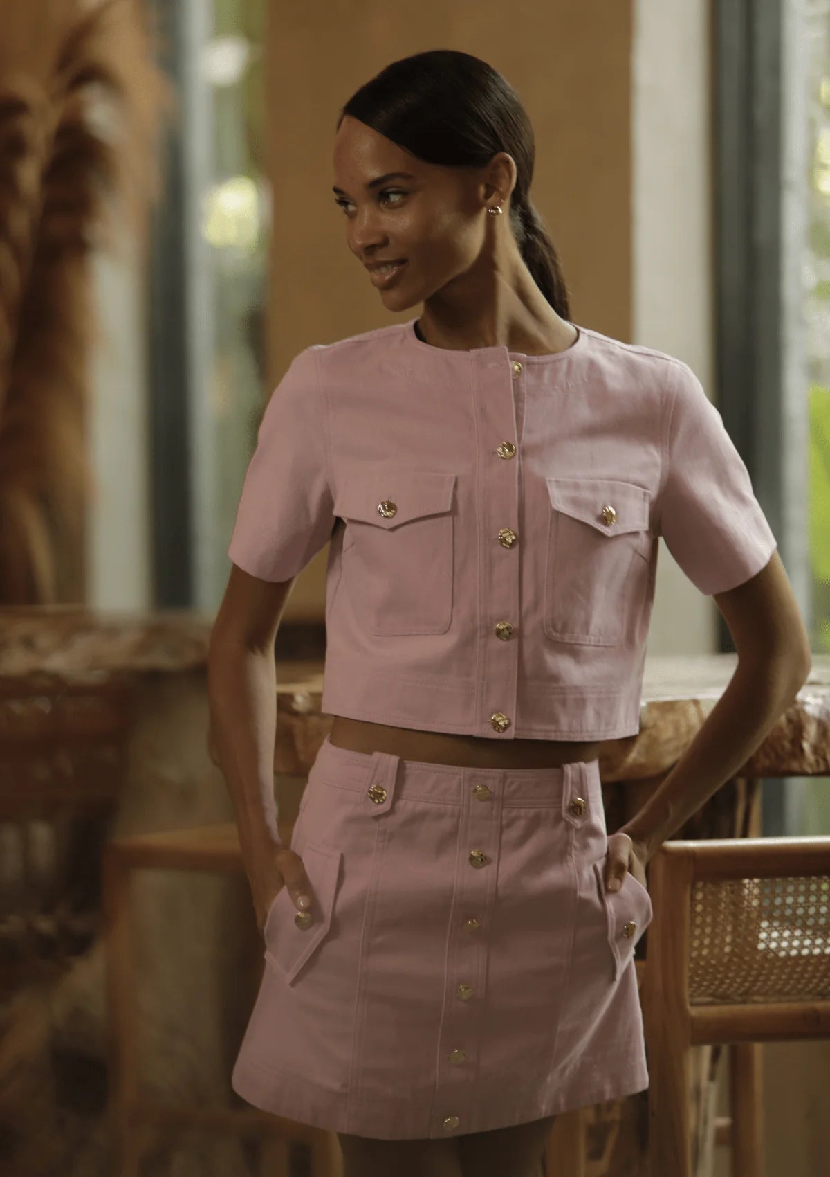 Woman wearing a pink outfit with gold buttons in an indoor setting
