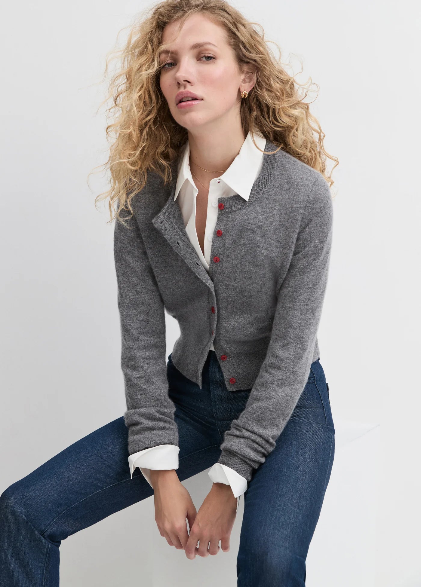 Woman wearing a gray cardigan with red buttons and jeans on a light gray background