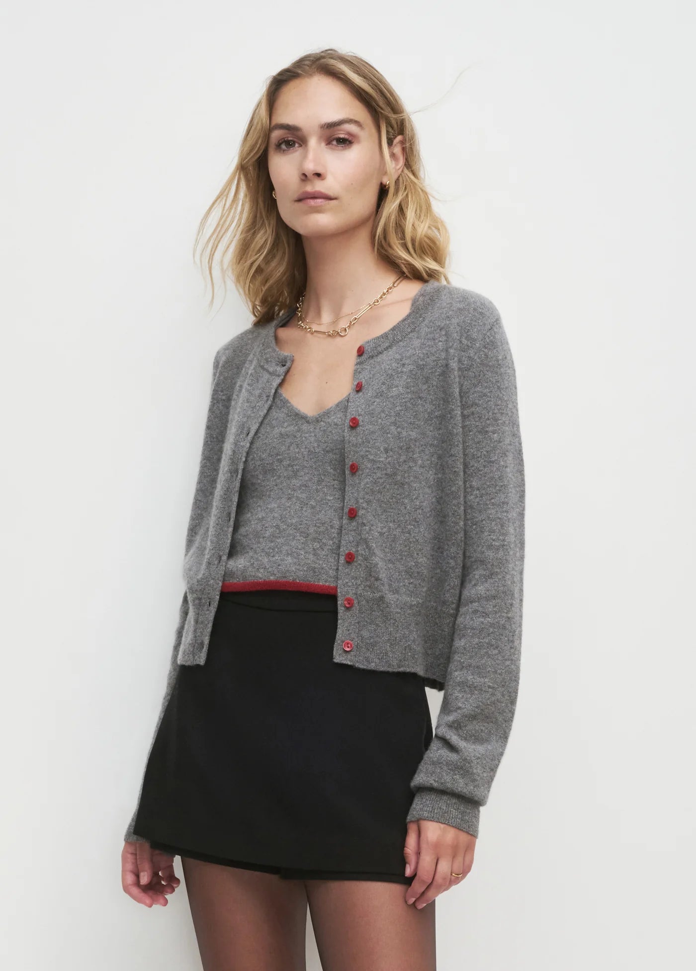 Woman wearing a gray cardigan with red buttons and matching tank over a black skirt on a white background