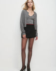 Woman wearing a gray cardigan, matching cami, black skirt, and black tights on a white background