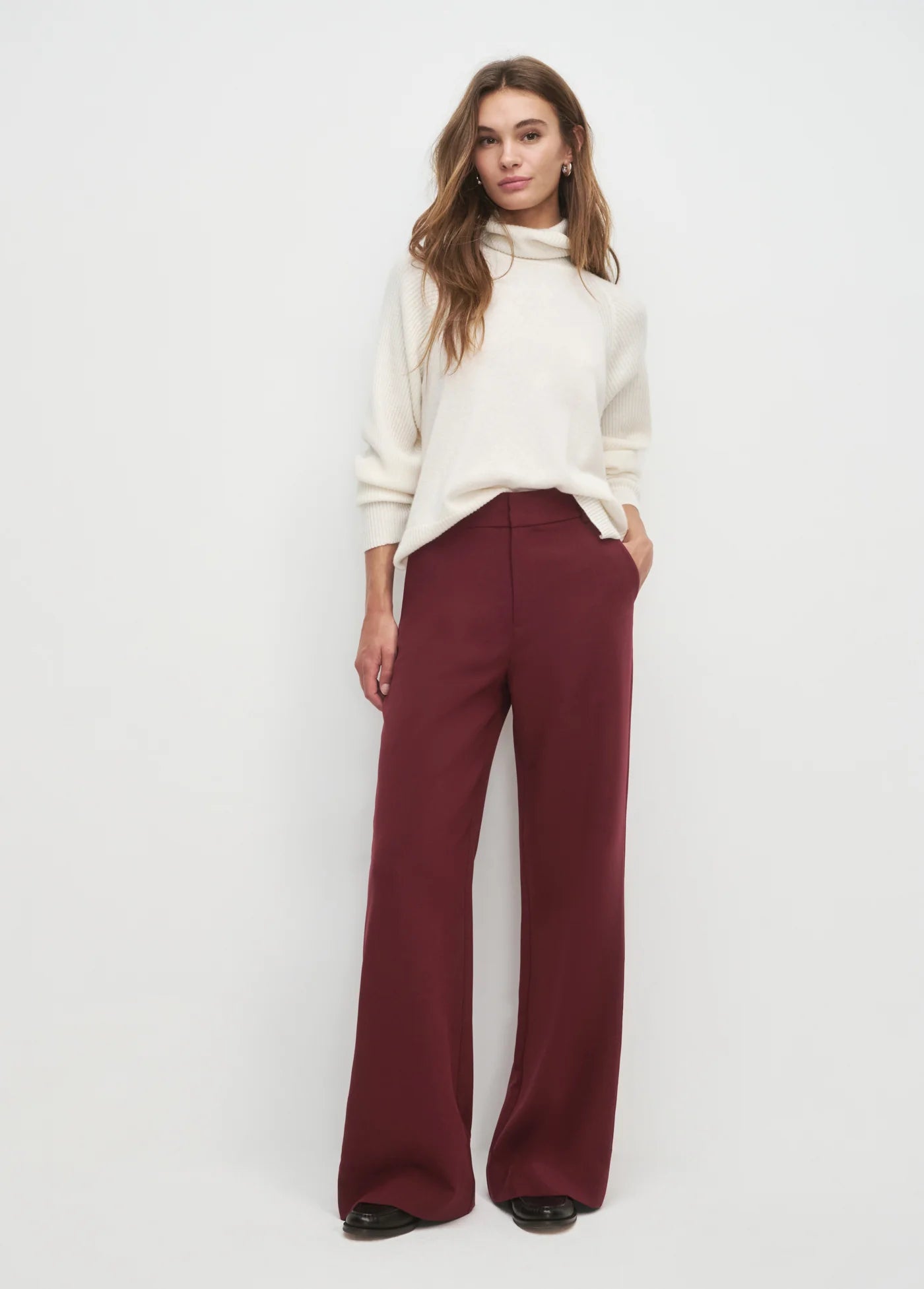 Woman wearing a white turtleneck sweater and burgundy pants on a white background