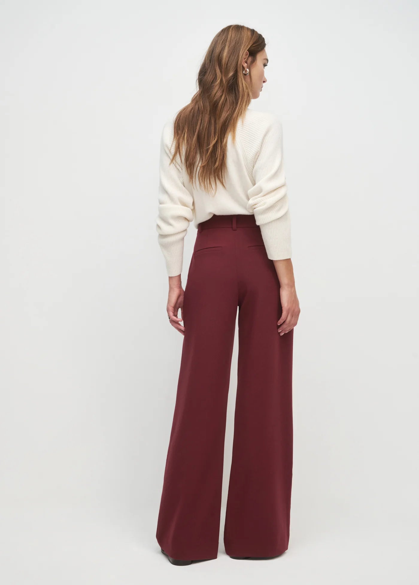 Woman wearing a white sweater and burgundy pants on a white background
