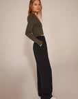 Woman wearing a green sweater and black pants against a beige background, side view