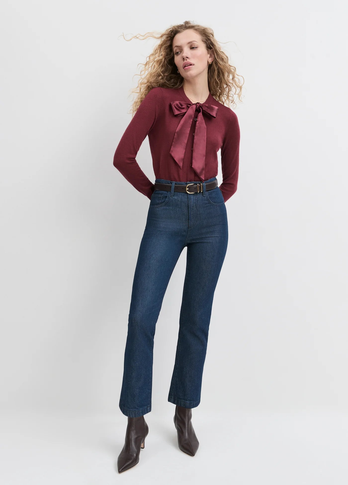 Woman wearing a burgundy blouse with a bow and blue jeans on a white background