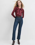 Woman wearing a burgundy blouse with a bow and blue jeans on a white background