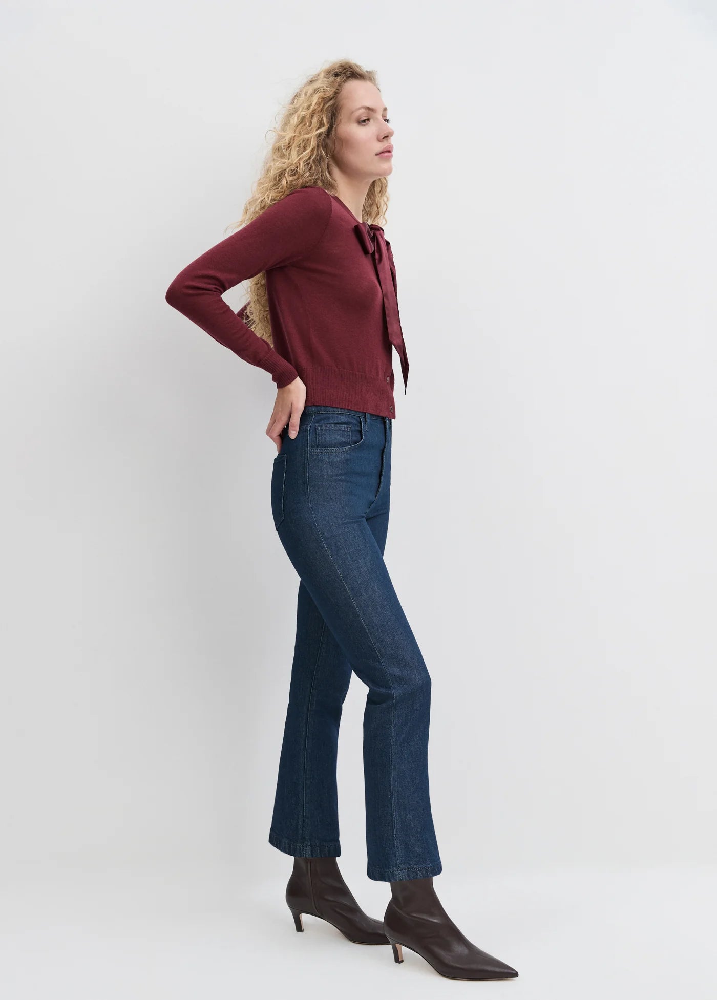 Woman wearing a burgundy sweater and blue jeans against a white background