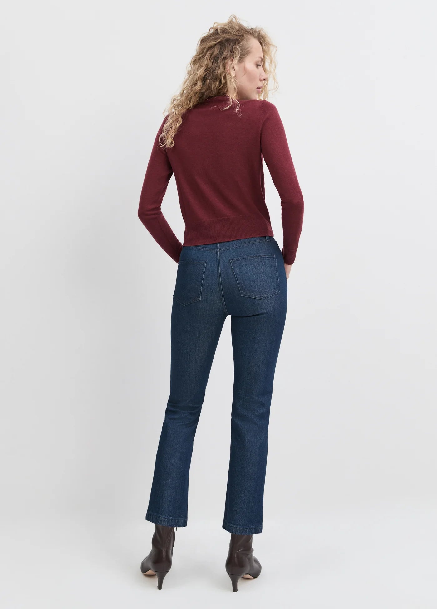 Woman wearing a burgundy sweater and blue jeans on a white background