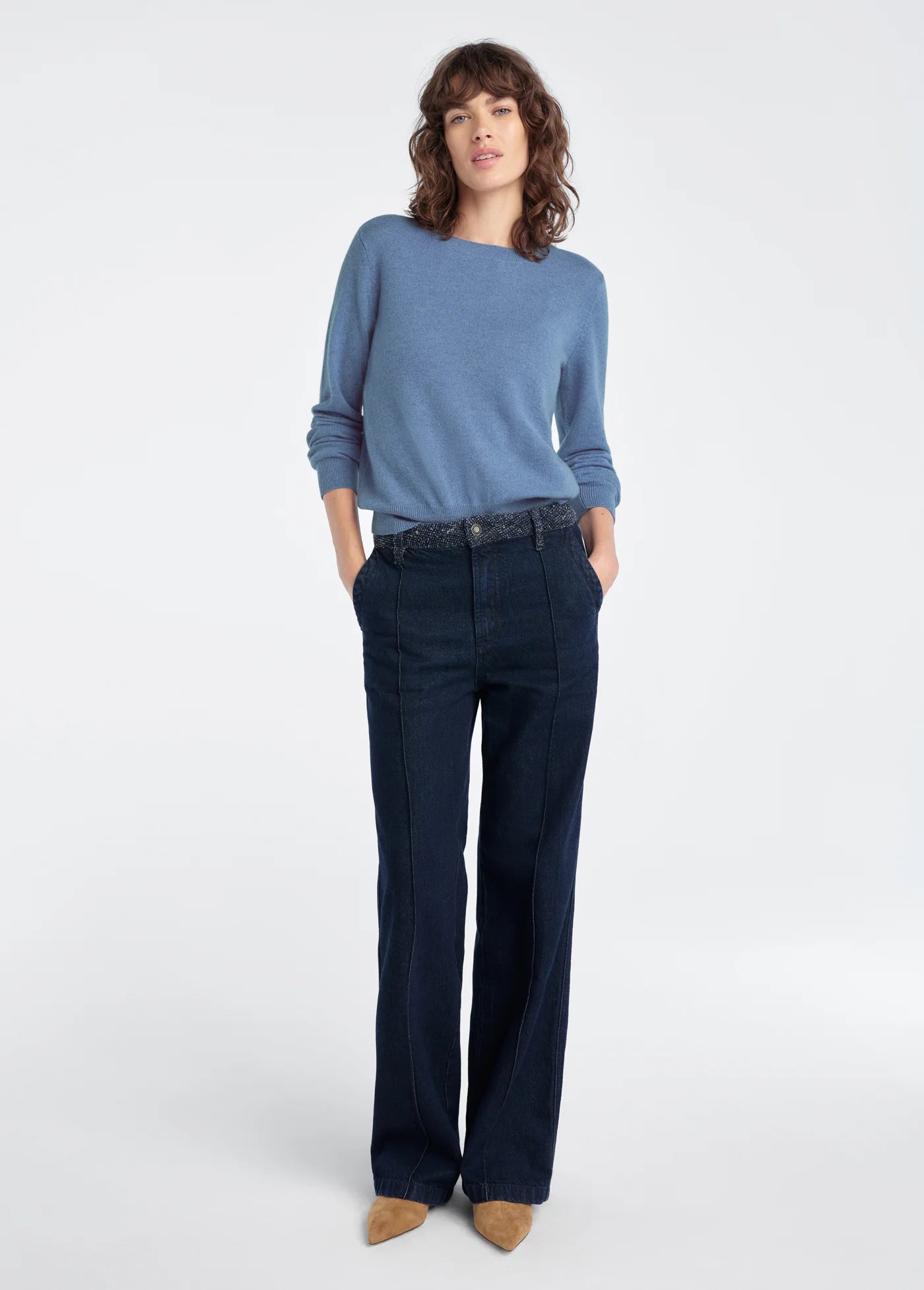Woman wearing a blue sweater and dark jeans on a white background
