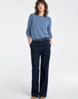 Woman wearing a blue sweater and dark jeans on a white background