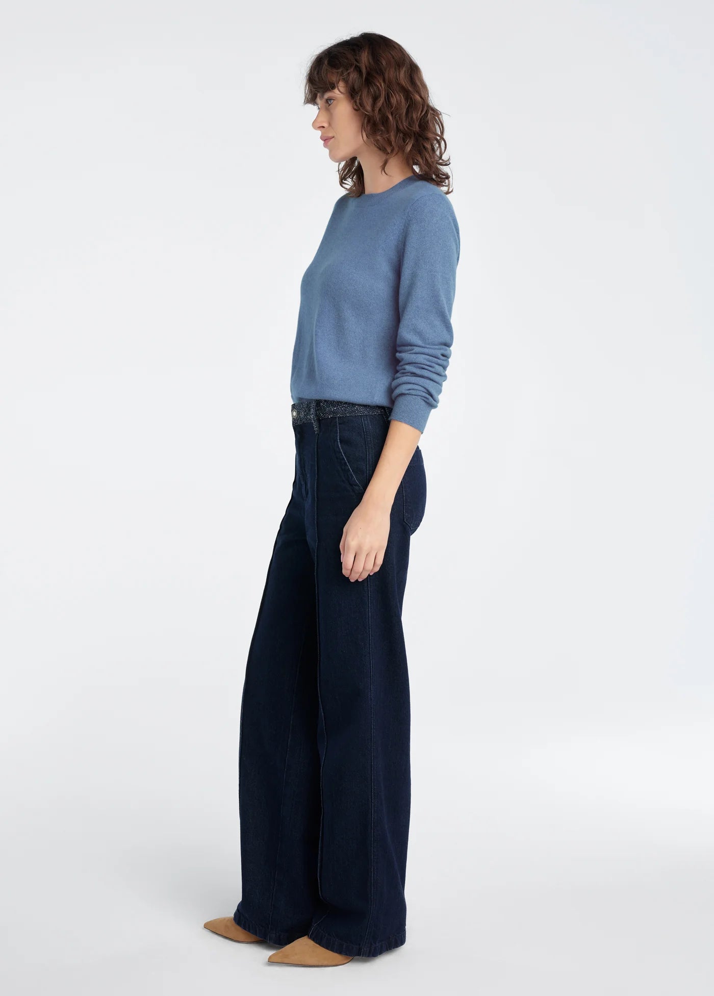 Woman wearing a blue sweater and dark blue wide-leg pants on a white background, side