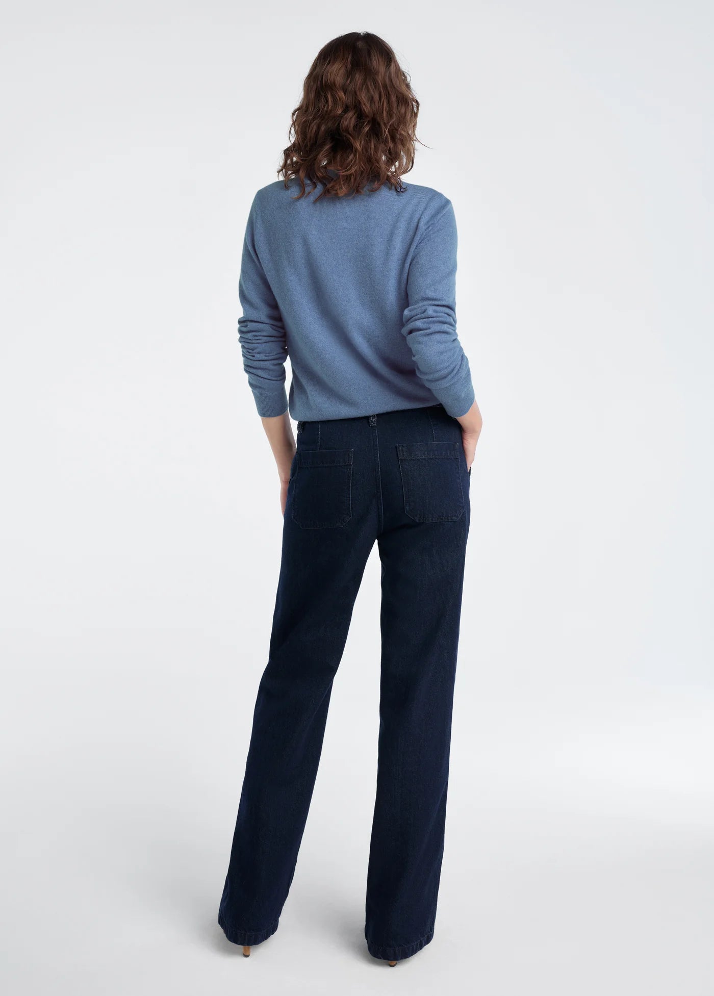 Person wearing a blue sweater and dark pants on a white background, back
