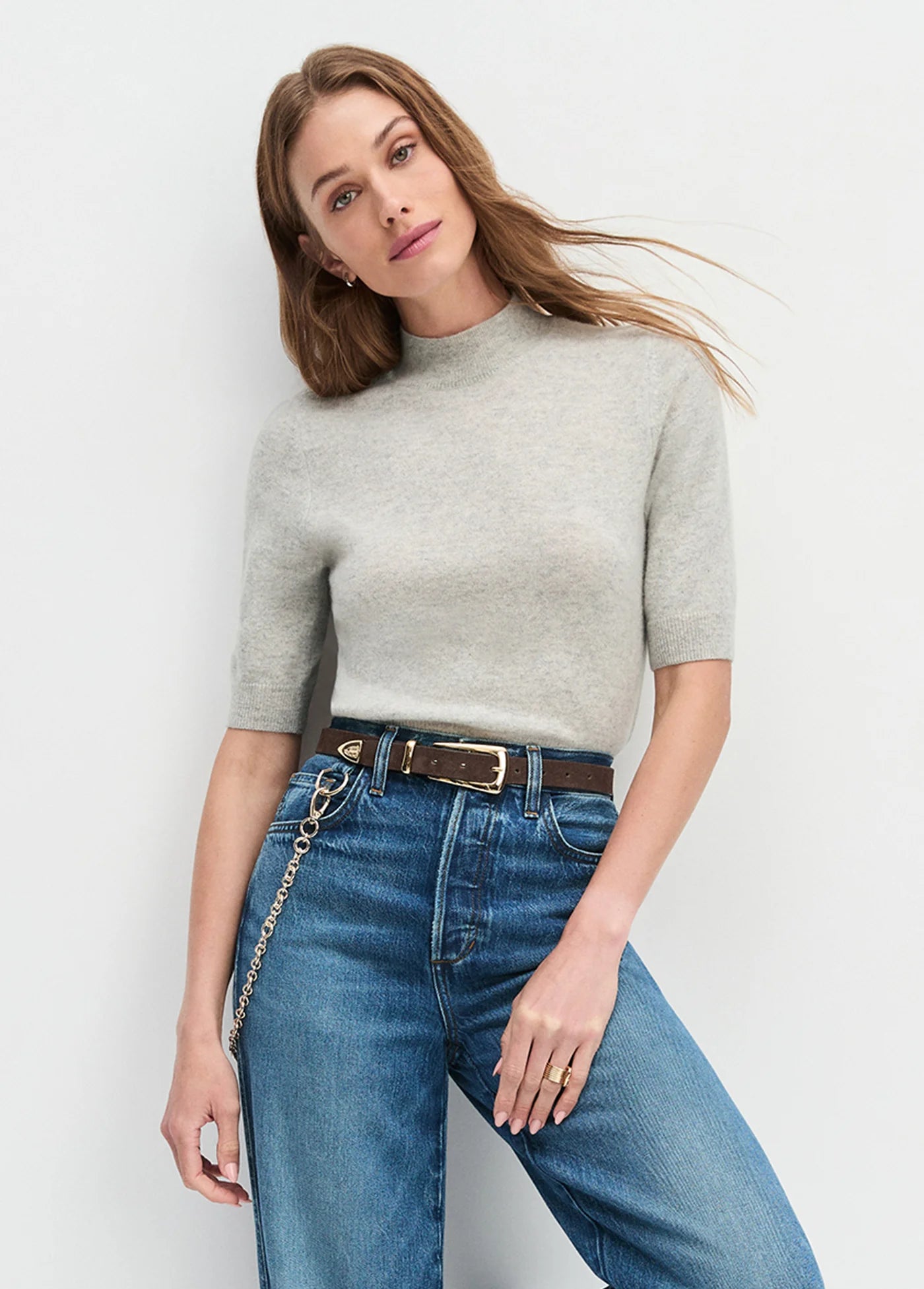 Woman wearing a gray sweater and blue jeans with The Suede Statement Belt in Chocolate against a white background