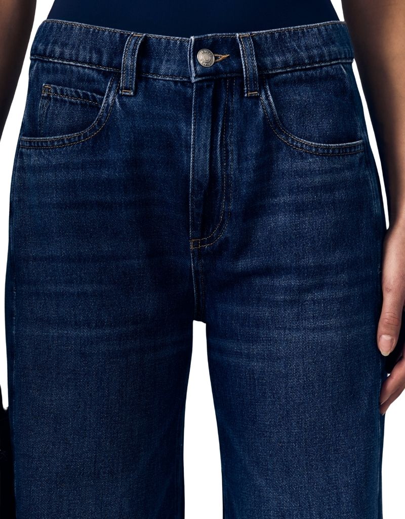Close-up of a person wearing dark blue denim jeans, showing the front waistband, belt loops, button, front pockets, and upper thighs against a plain white background.