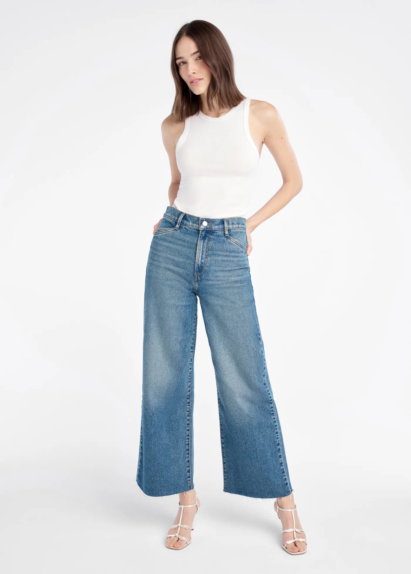 Woman wearing a white sleeveless top and blue jeans on a white background full body view